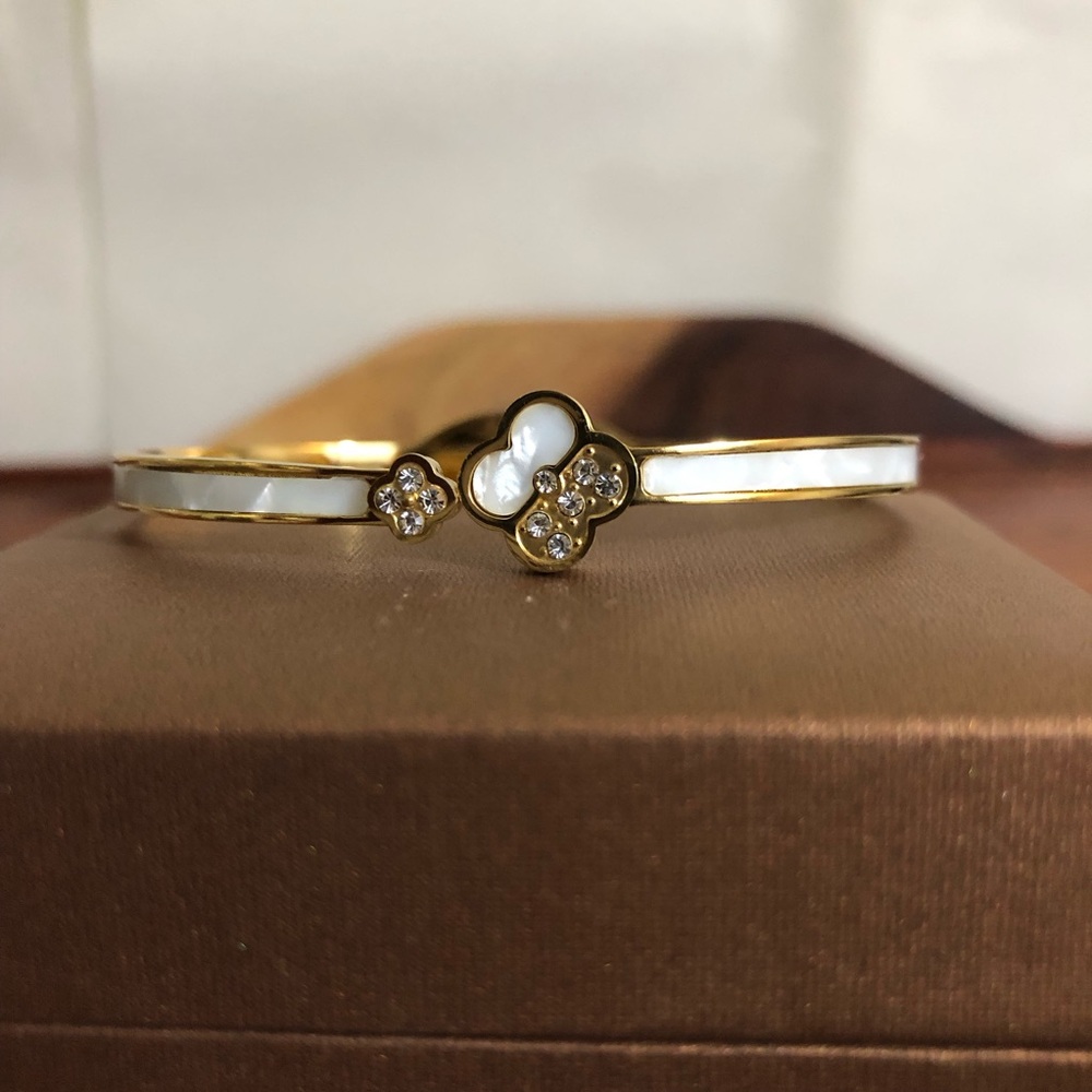 gold-toned hinged bangle bracelet featuring white clover motifs and crystal New